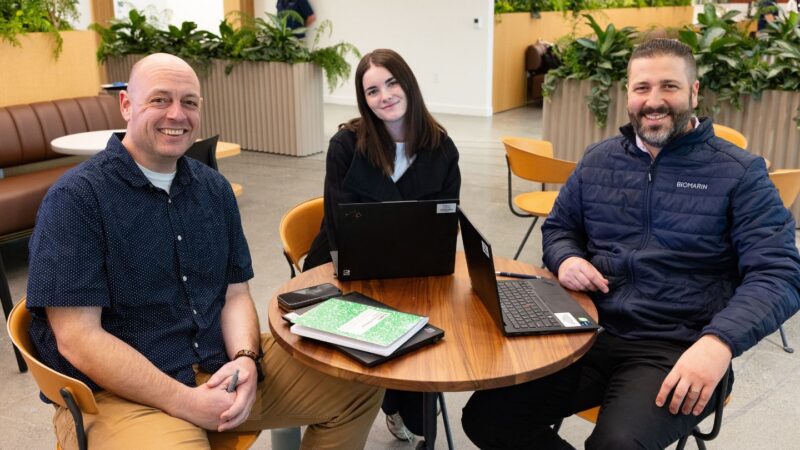 Image of 3 employees smiling around a desk